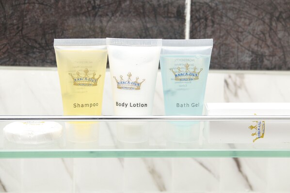 Three toiletries on a glass shelf: a yellow shampoo, a white body lotion, and a blue bath gel.