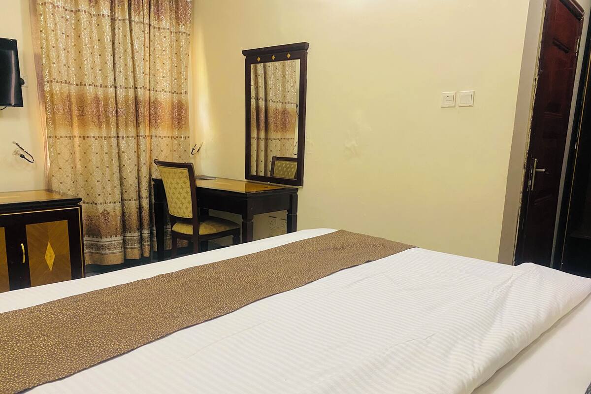 A hotel room with a bed, a desk, a chair, a mirror, and a television.