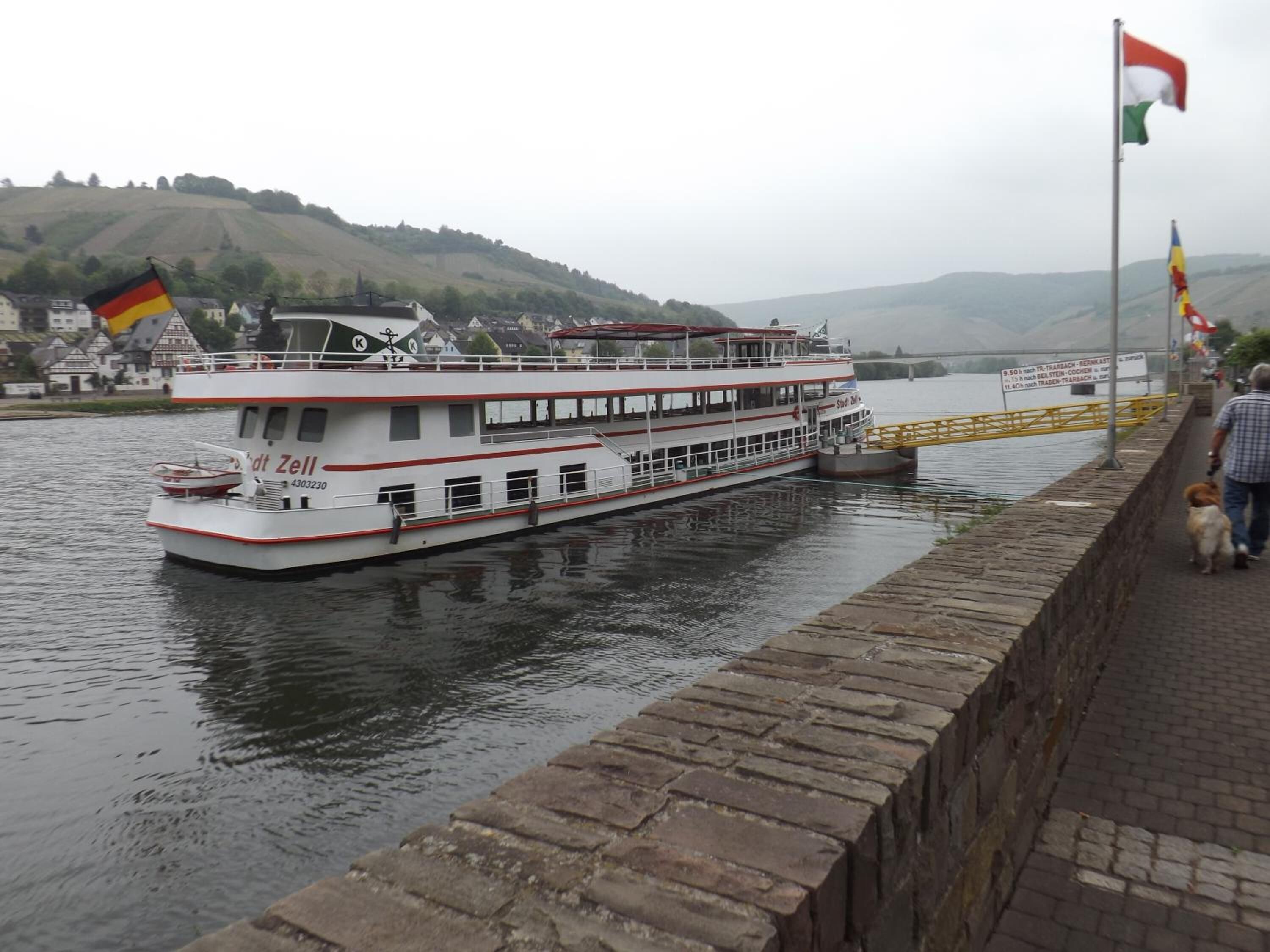 A riverboat docked at a pier with a stone walkway beside it.