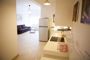 A modern kitchen with a refrigerator, stove, and sink. There is a dining area with a couch and a table.