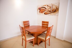 A round wooden dining table with four chairs, a wall-mounted abstract painting, and a tiled floor.