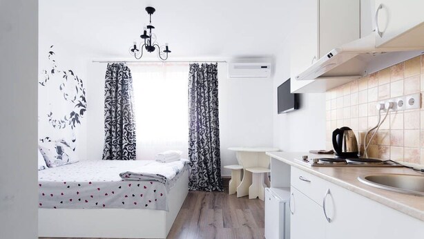 A compact bedroom with a bed, a bedside table, and a window with patterned curtains. Adjacent to the bedroom is a kitchenette with a sink, a stove, and a small countertop. - Potemkin's Favorite Suites (Odesa)