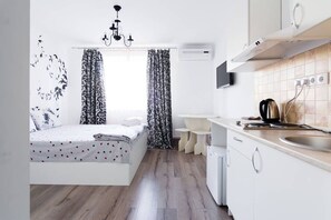 A compact bedroom with a bed, a bedside table, and a window with patterned curtains. Adjacent to the bedroom is a kitchenette with a sink, a stove, and a small countertop. - Potemkin's Favorite Suites (Odesa)