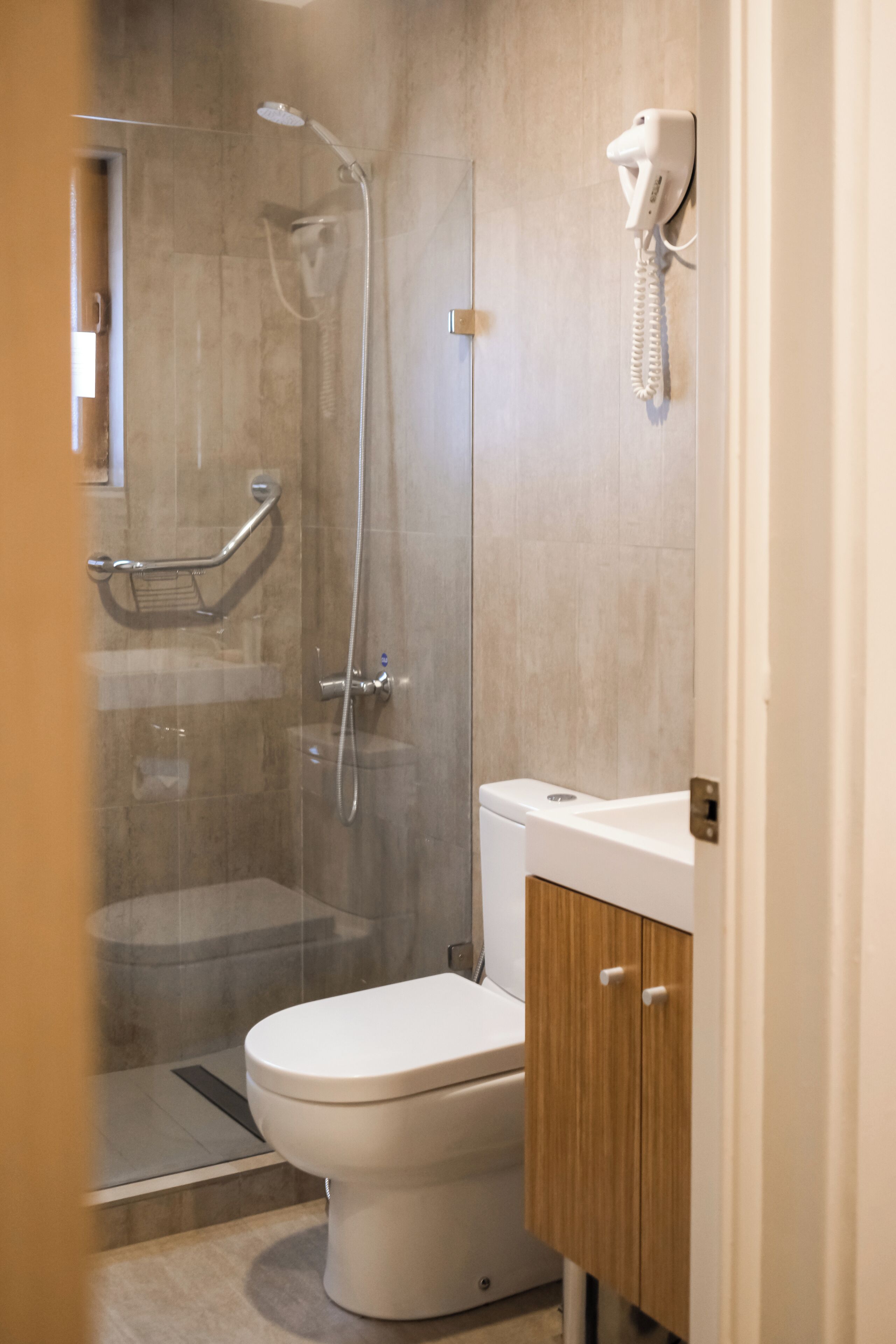A modern bathroom with a glass-enclosed shower, a toilet, and a vanity with a wooden cabinet.