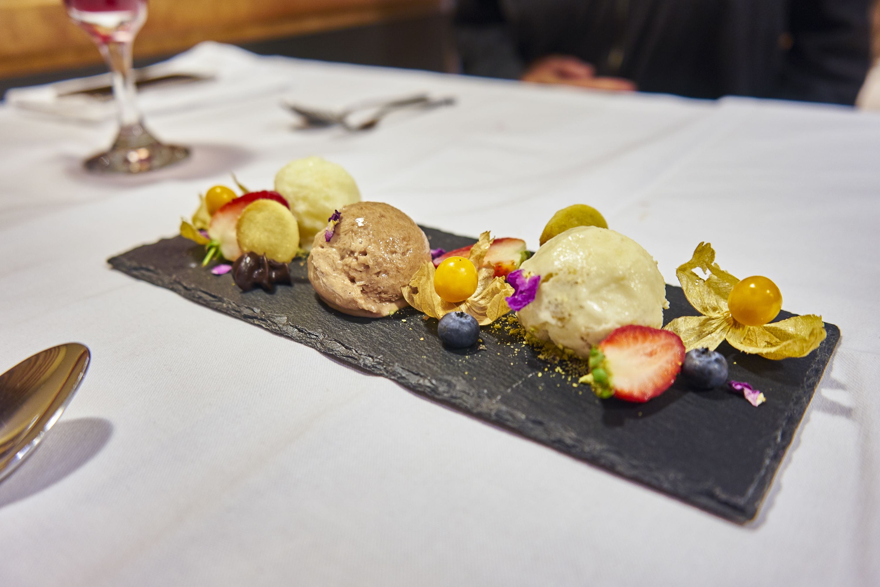 Une assiette de dessert avec divers fruits et de la glace, présentée sur une planche de service en ardoise.