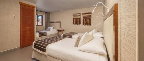 A hotel room with two beds, a wooden wardrobe, a bedside table with a lamp, and a window with curtains.