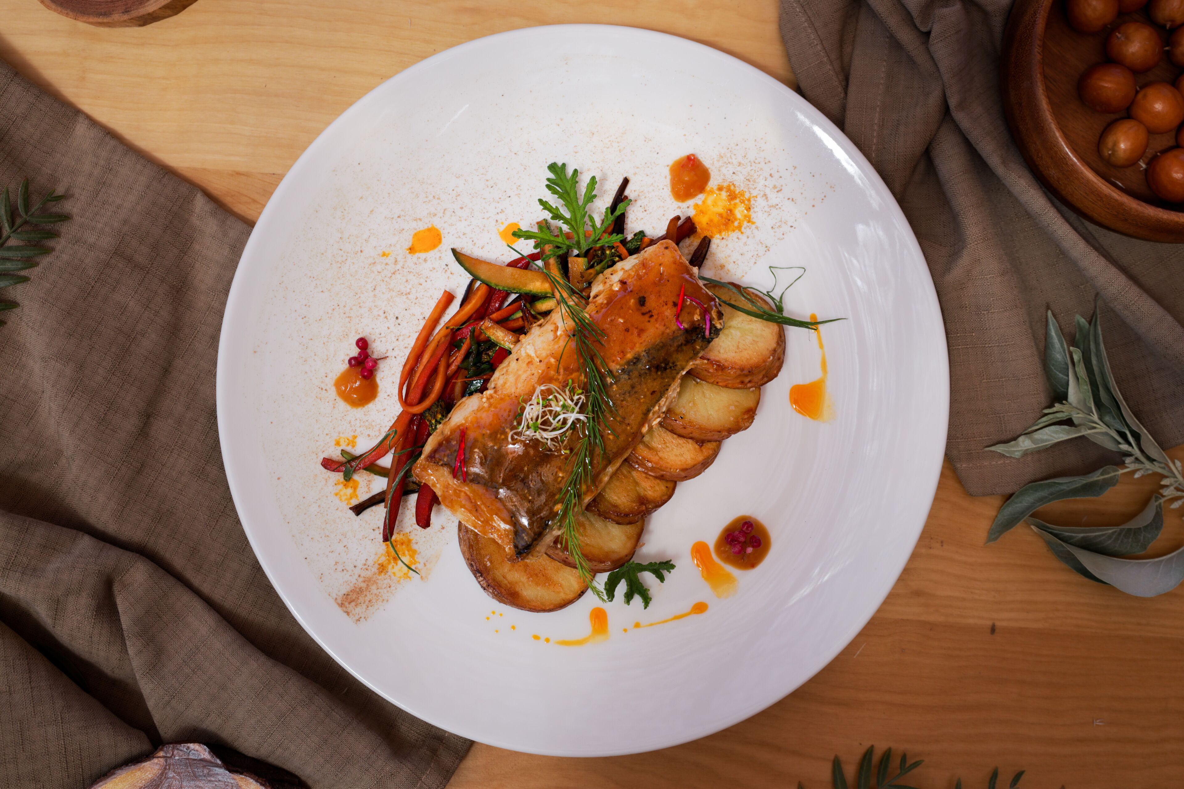 Une assiette blanche contenant un filet de poisson, des légumes et une sauce, le tout posé sur une table en bois.