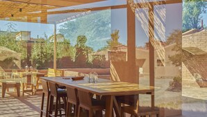 An outdoor dining area with wooden tables and chairs, large windows, and a view of the surrounding landscape.