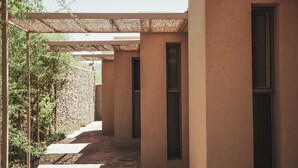 A corridor with a stone floor, beige walls, and a pergola with a woven roof.