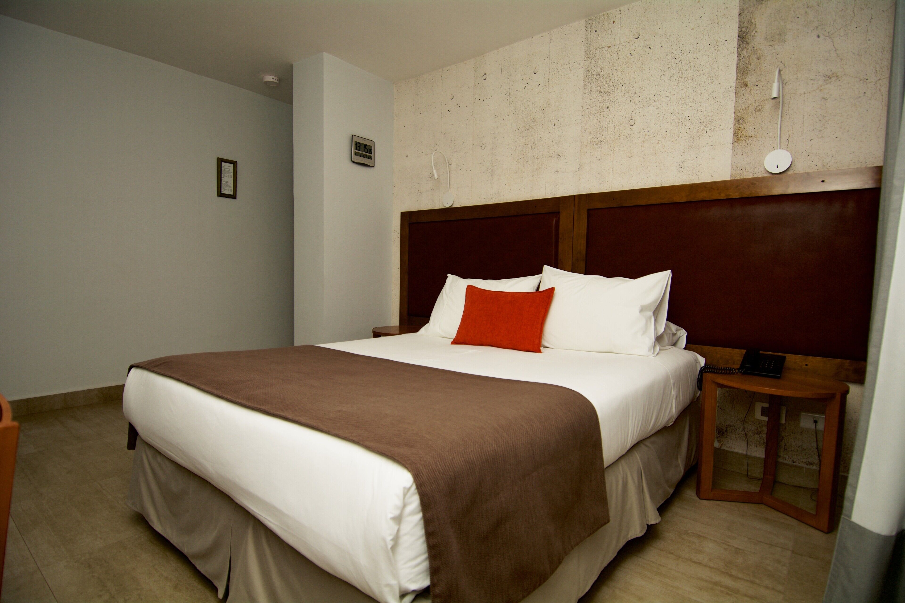 A hotel room with a large bed, a wooden headboard, a nightstand, and a wall clock.