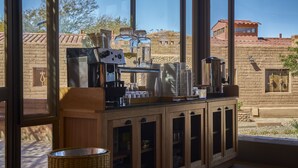 A kitchen with a coffee machine, jars, and a view of a brick building through large windows.