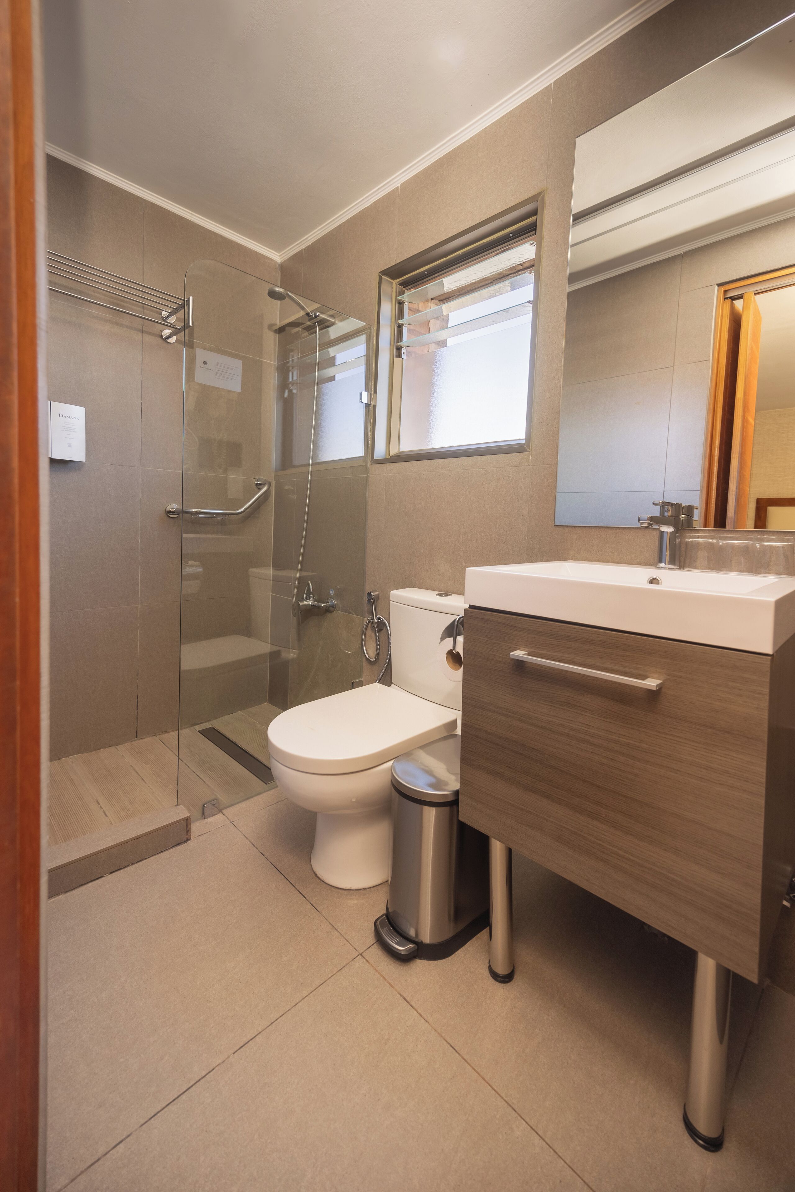 A modern bathroom with a glass-enclosed shower, a white toilet, a wooden vanity with a sink, and a mirror above the vanity.