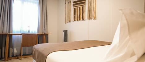 A hotel room with a bed, a desk, and a window with curtains.