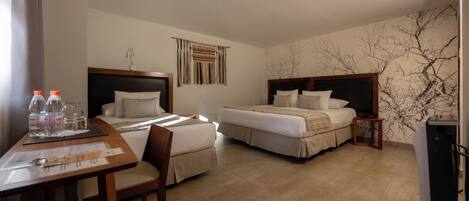 A hotel room with two beds, a desk with a chair, a small table, and a TV.