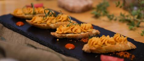 A black slate serving board with three pieces of bread topped with a creamy spread, garnished with green herbs, and accompanied by a small dollop of red sauce.
