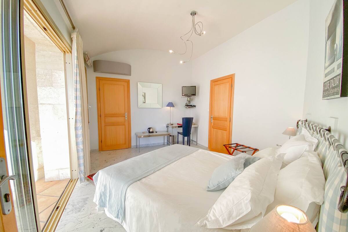 Ein Schlafzimmer mit einem großen Bett, einem Schreibtisch mit Stuhl, einem Fernseher und einer Tür zu einem anderen Raum.