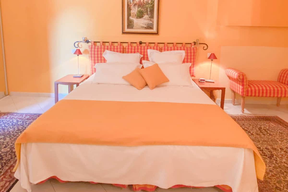 Ein Hotelzimmer mit einem großen Bett, zwei Nachttischen, einem Sessel, einem Bild an der Wand und einem gemusterten Teppich.