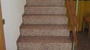 A staircase with a wooden handrail and a yellow curtain at the bottom. - Pension Egg (Hospental)