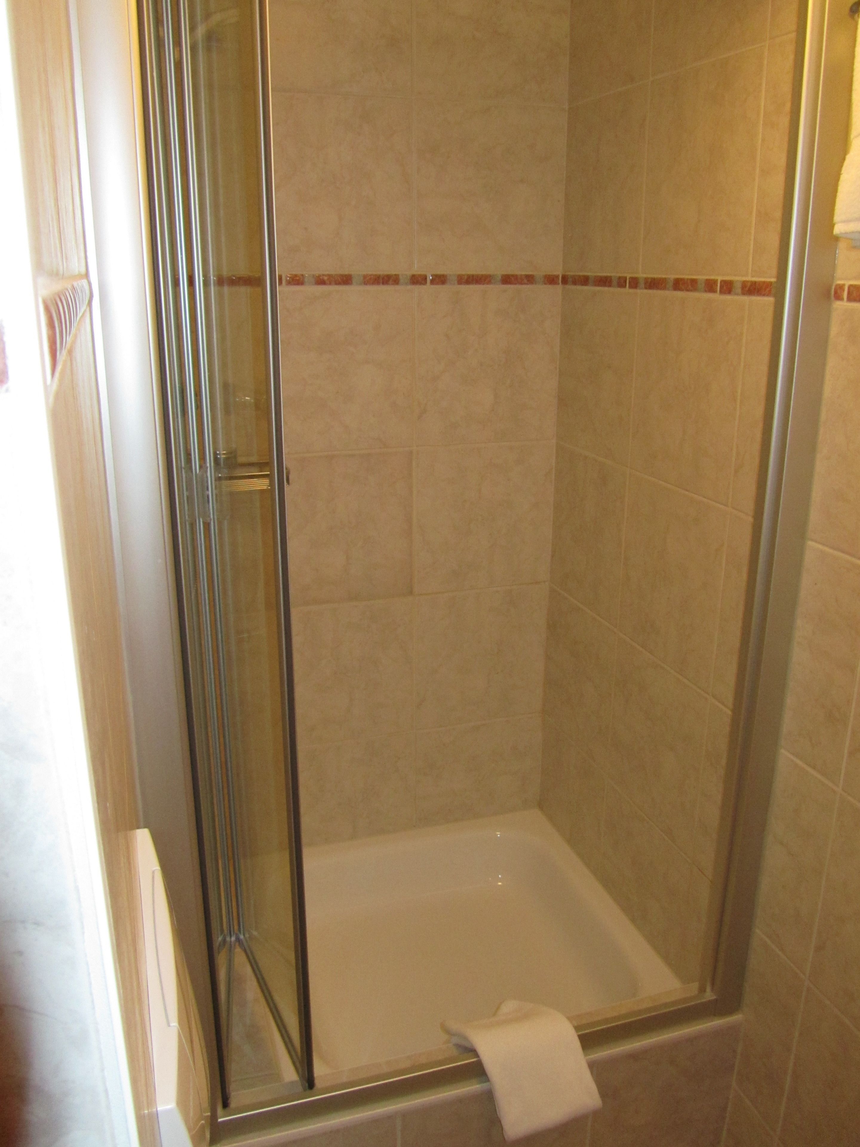 A glass-enclosed shower with a white bathtub and a towel hanging on the door.