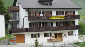 A two-story building with balconies, a sign reading "HOTEL PENSION EGG," and a sign for "Chez' Joggi." - Pension Egg (Hospental)