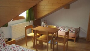 A small, cozy room with a wooden table and chairs, a bed with floral bedding, and a slanted ceiling. - Pension Egg (Hospental)