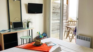 Een hotelkamer met een bed, een bureau met een laptop, een televisie, een stoel, een tafel en een balkon met uitzicht.