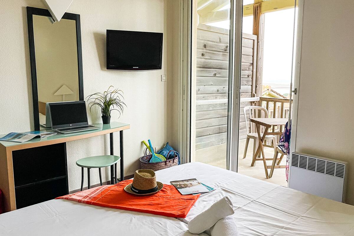 Une chambre d’hôtel avec un lit, un bureau avec un ordinateur portable, une télévision, une chaise, une table et un balcon avec vue.