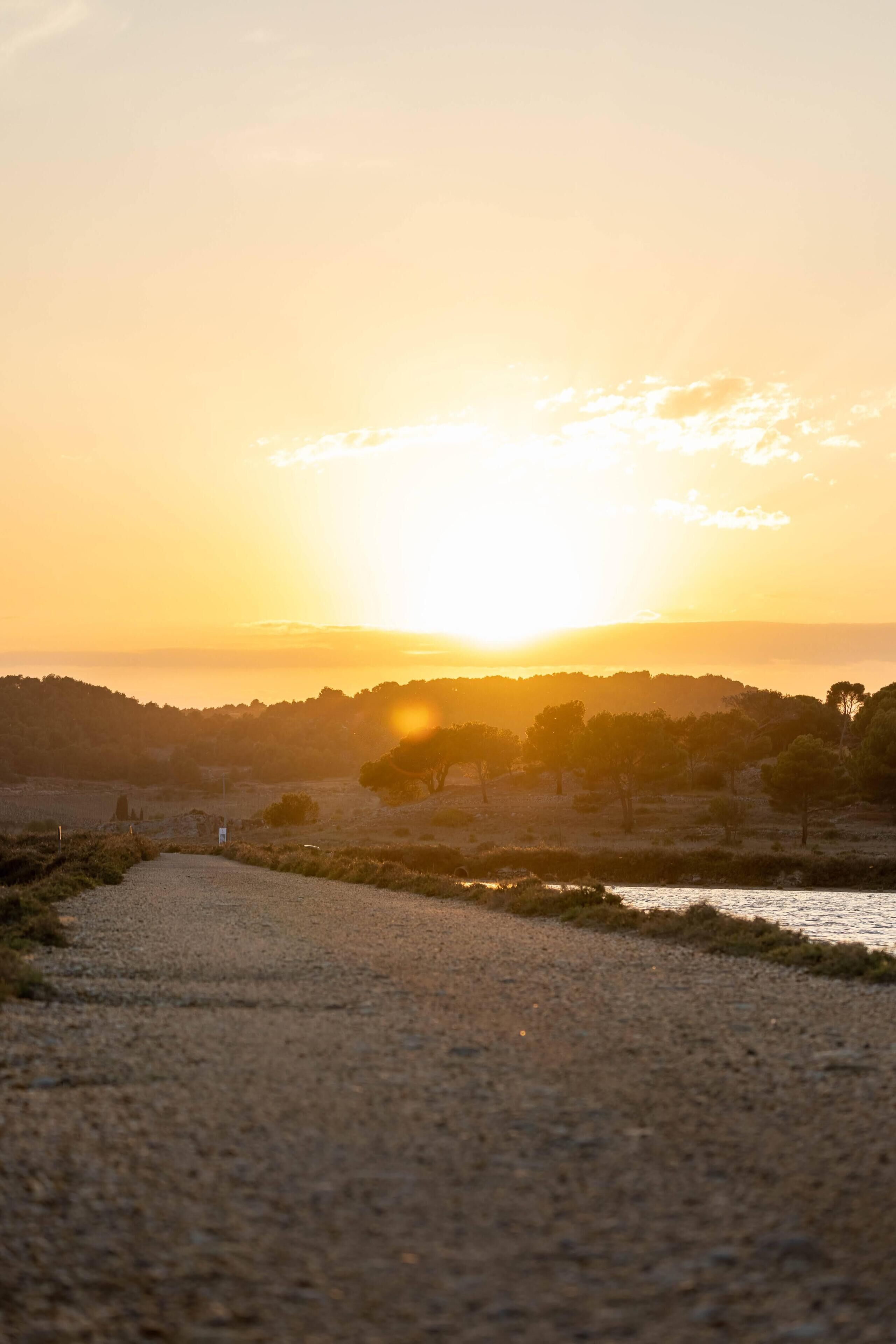 Ein Sonnenuntergang über einer Küstenlandschaft, ein Kiesweg führt zum Wasser.