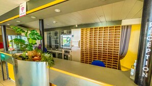Een receptiegedeelte met een balie, een plant, een bordje met wifi-aanduiding en een muur met een rasterpatroon.