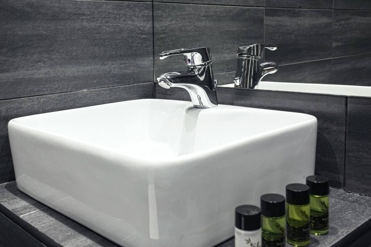 A bathroom with a white sink, two chrome faucets, and three green bottles on the counter.