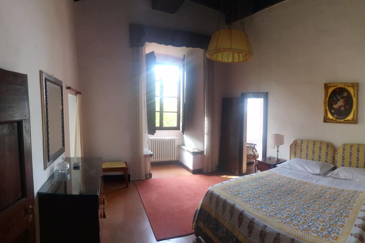 Un dormitorio con una cama grande, un aparador de madera, un espejo, un radiador y una ventana con cortinas.