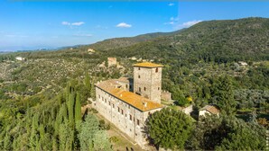 A stone building with a tower, surrounded by trees and hills. - Castello di Mugnana (Greve in Chianti)