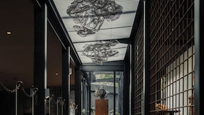 A corridor with a central sculpture, black railings, and a patterned ceiling. - Silverback Lodge (Bwindi)