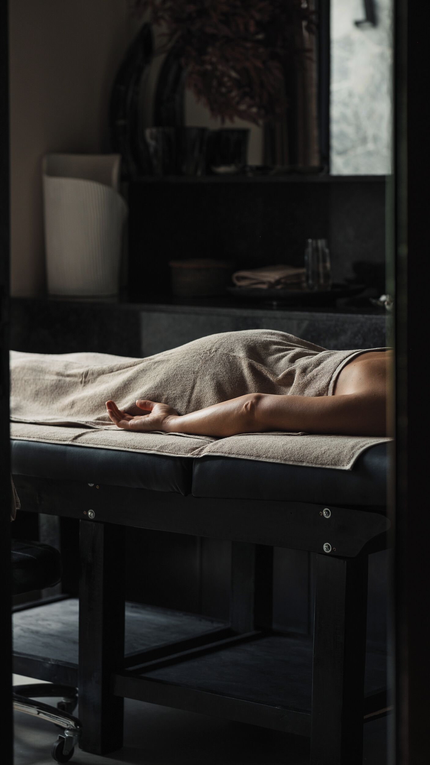 Eine Person liegt auf einer Massageliege in einem schwach beleuchteten Raum mit einem Fenster im Hintergrund.