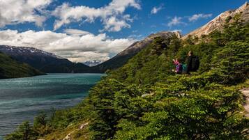 A mountainous landscape with a lake, trees, and two people hiking.
