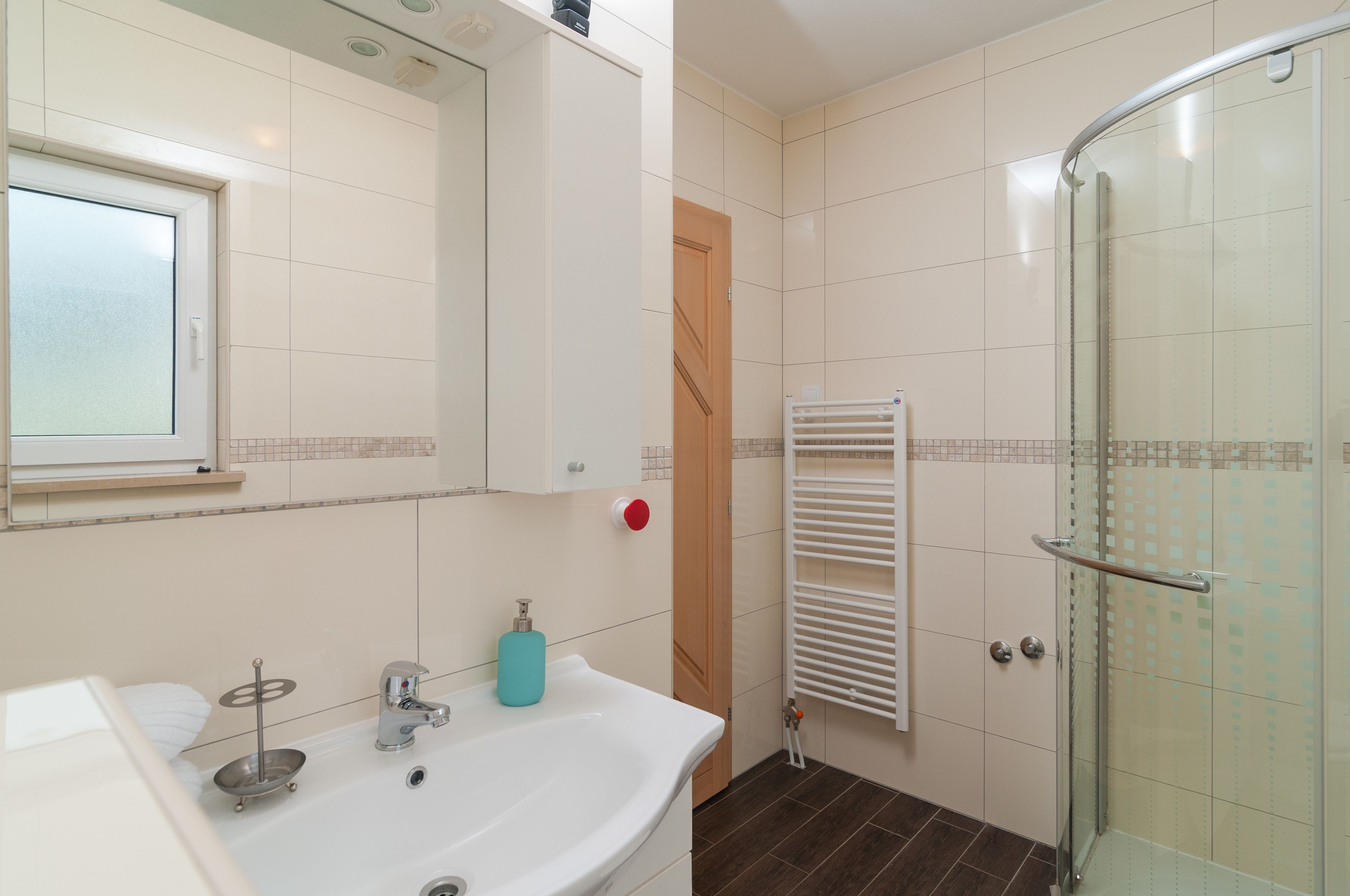 Un baño con lavamanos blanco, espejo, cabina de ducha de vidrio y toallero.