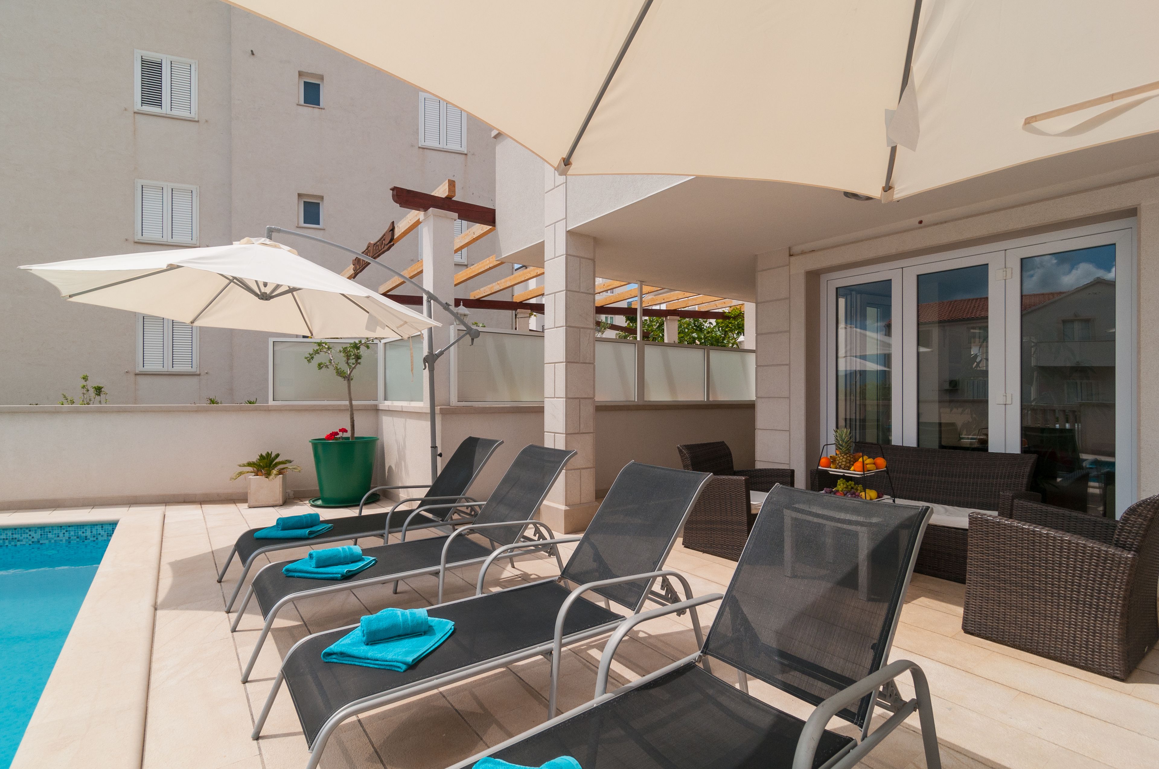 A poolside area with lounge chairs, a table, and umbrellas.