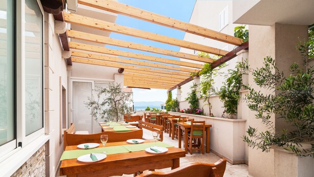 An outdoor dining area with wooden tables and chairs, a pergola overhead, and potted plants. - Villa Juraj (Bol)