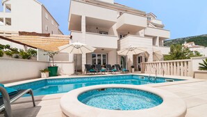 A swimming pool with lounge chairs and umbrellas, a hot tub, and a building with balconies. - Villa Juraj (Bol)