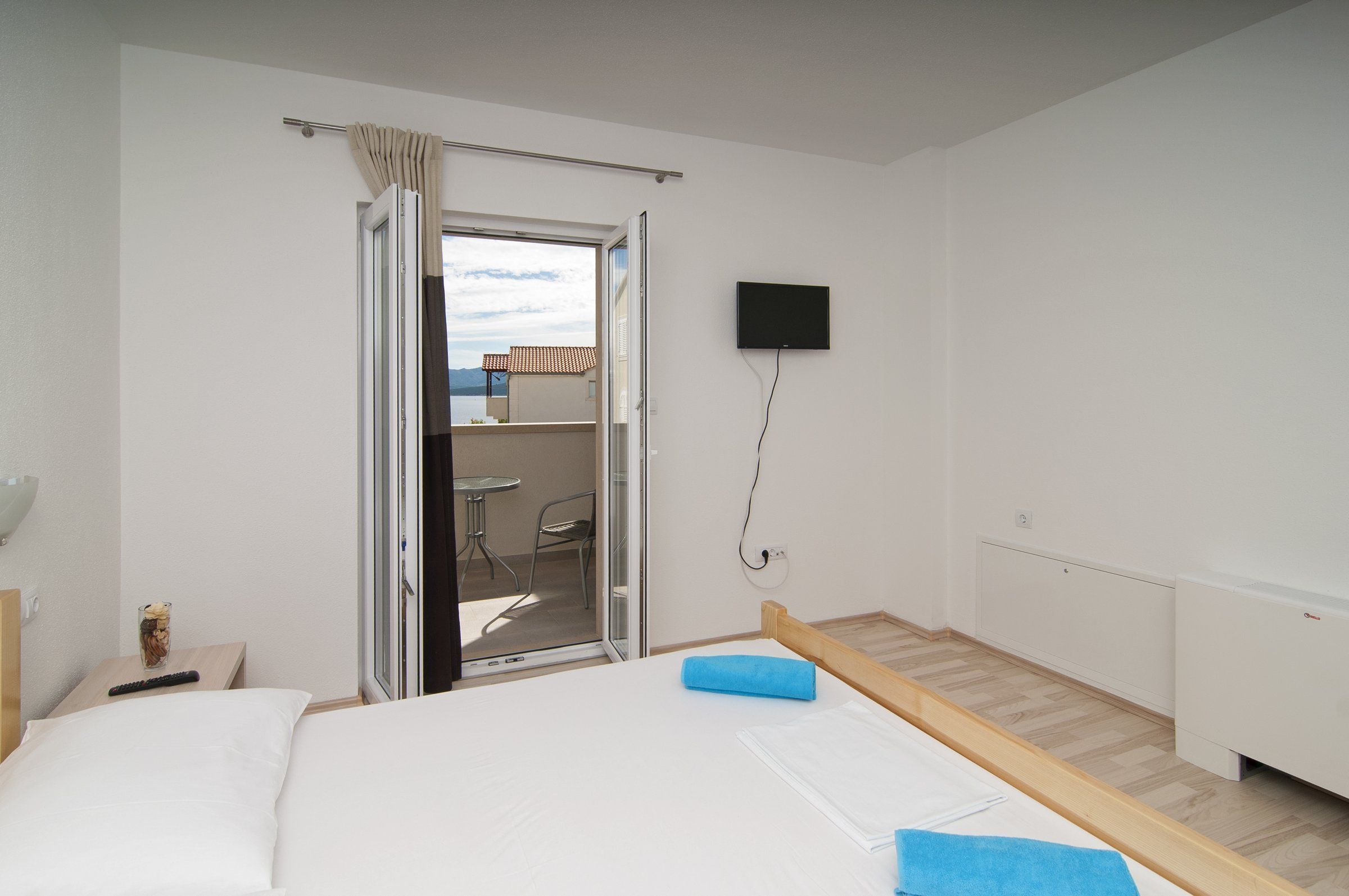 A hotel room with a bed, a TV mounted on the wall, a window with curtains, and a view of the outside.
