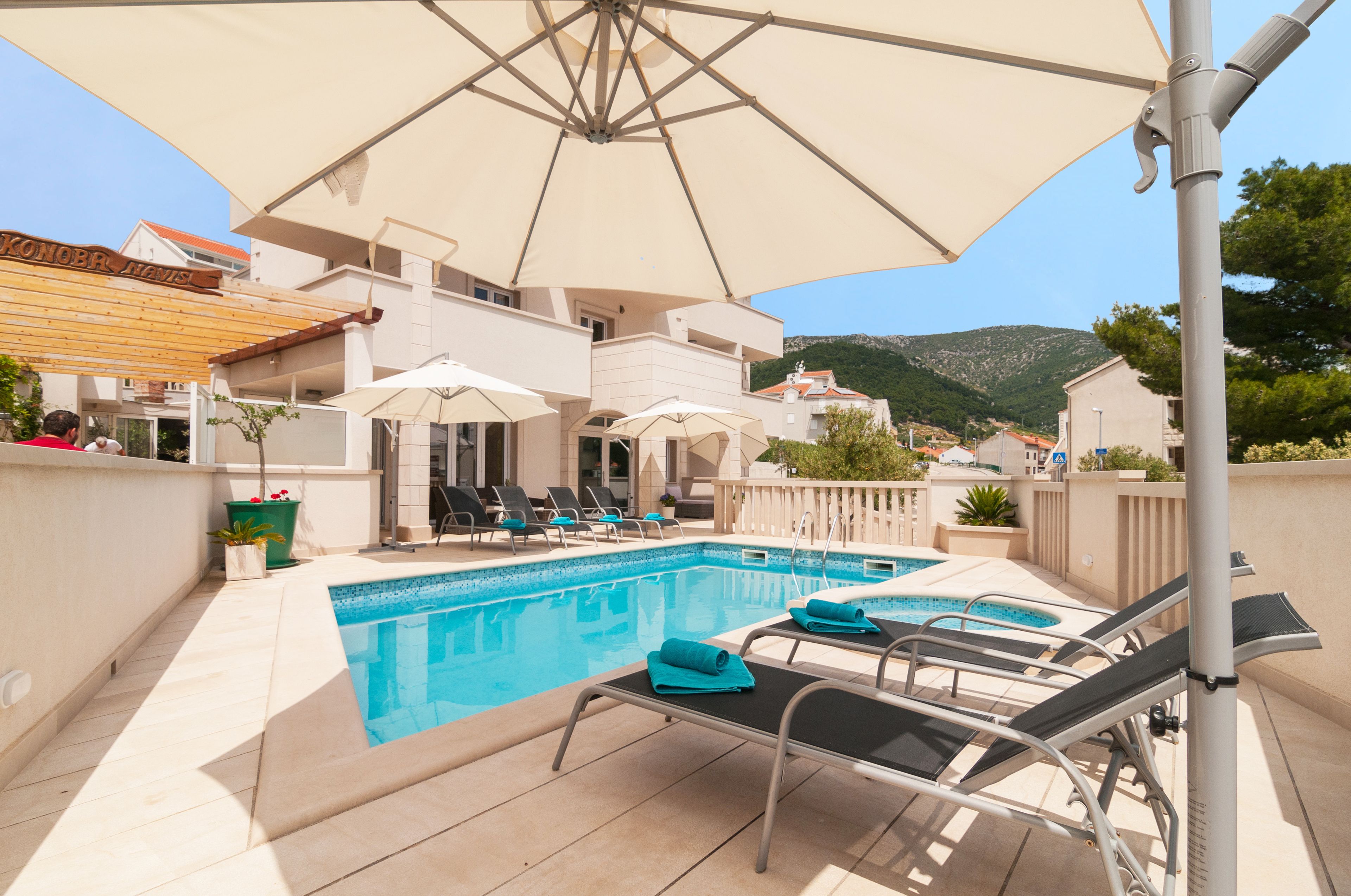 A pool area with lounge chairs and umbrellas, a clear sky, and a mountainous backdrop.