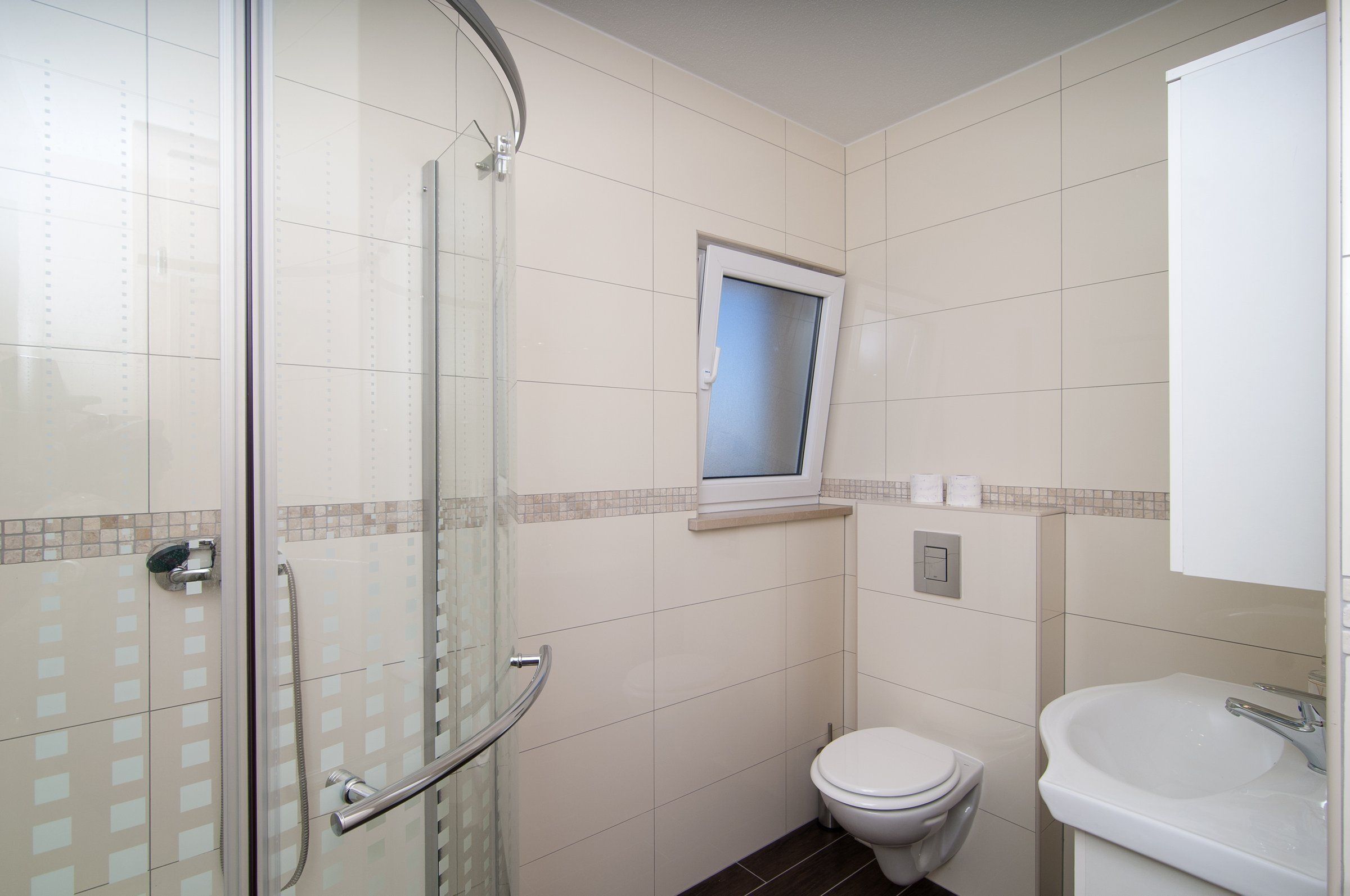 A small, modern bathroom with a glass shower enclosure, a toilet, and a sink.