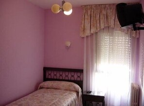 A bedroom with a bed, a nightstand, a wall-mounted lamp, and a window with curtains. - Hostal Restaurante Torremar (Medinaceli)