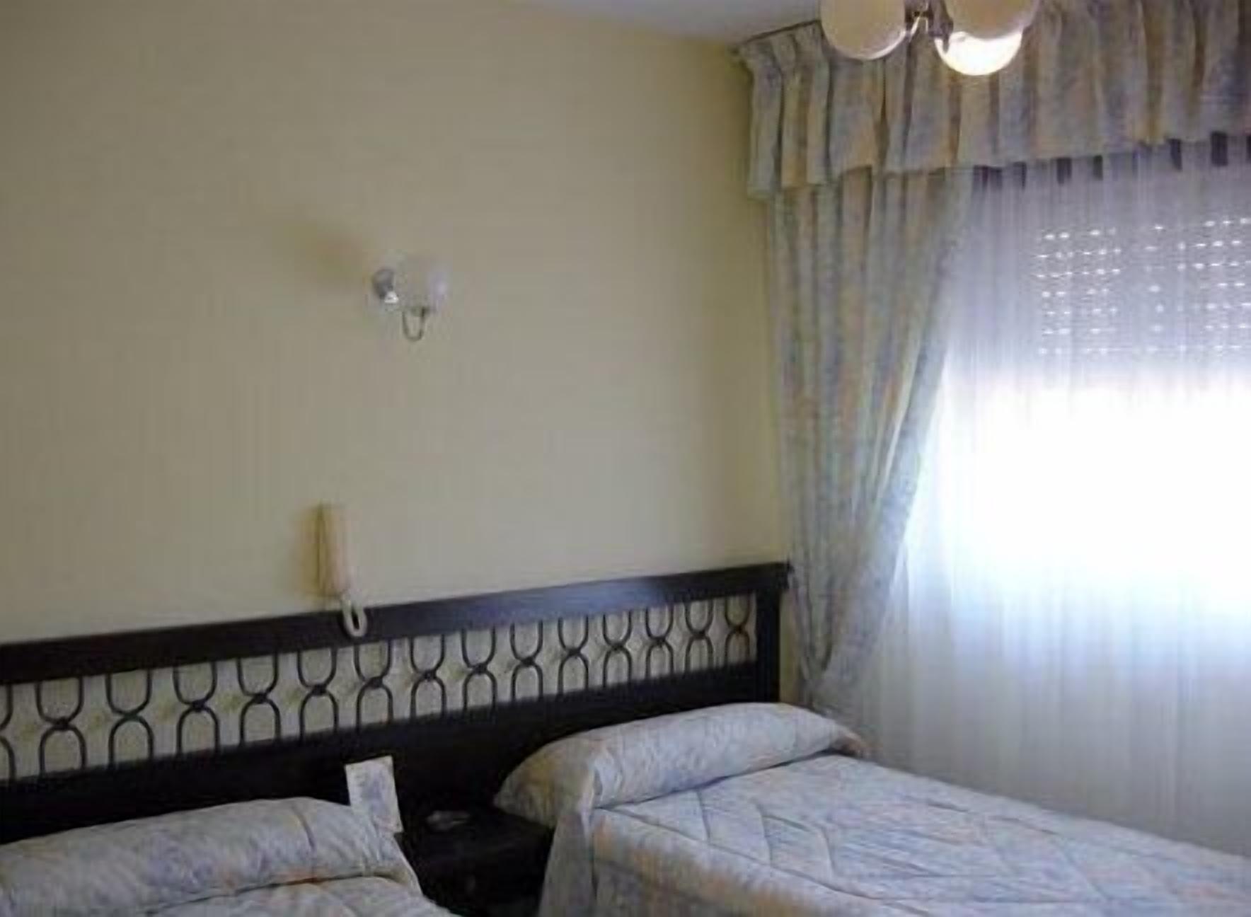 A hotel room with a bed, a bedside table, a telephone, and a window with curtains.