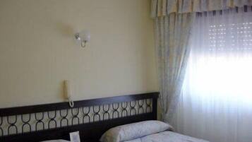 A hotel room with a bed, a bedside table, a telephone, and a window with curtains.