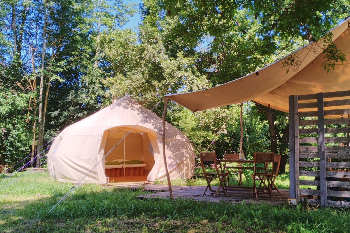Una carpa con toldo, una mesa de madera y sillas en un área boscosa.