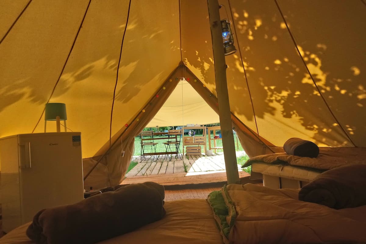 Una tienda de campaña con un rincón para dormir, un refrigerador pequeño y vistas a un espacio al aire libre con mesas y sillas.