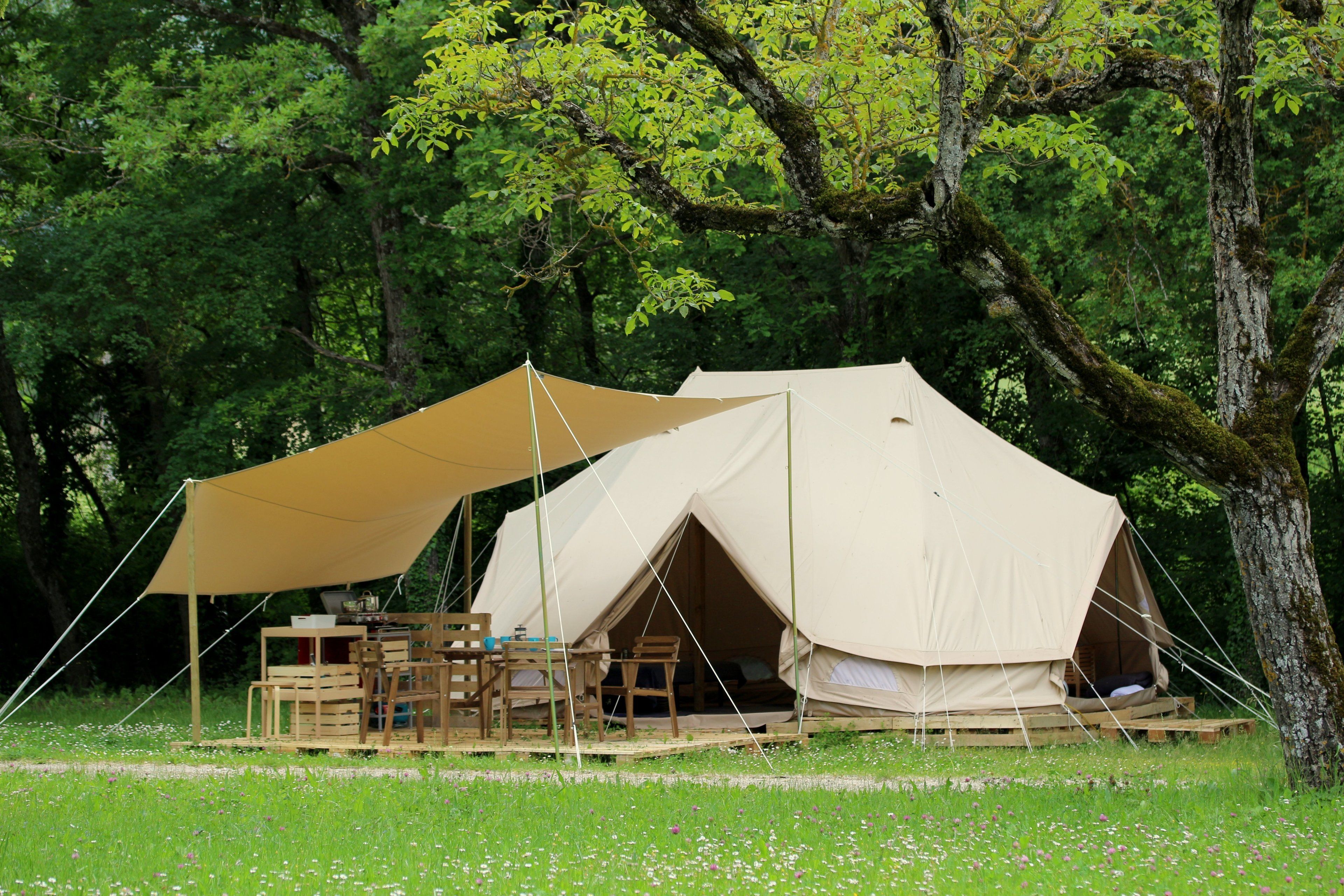 A tent with a table and chairs set up in a grassy area surrounded by trees.