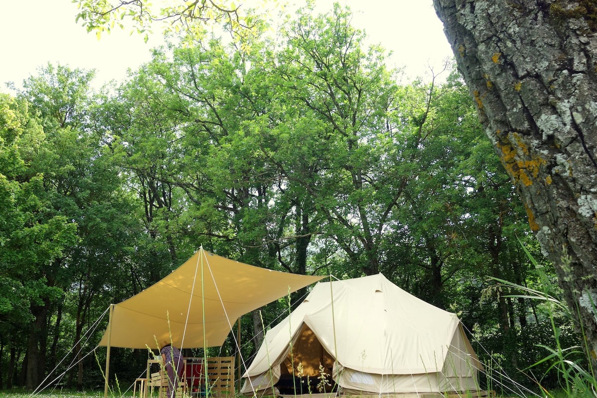 Tienda de campaña montada en un bosque, con un dosel grande y otra tienda más pequeña cerca.
