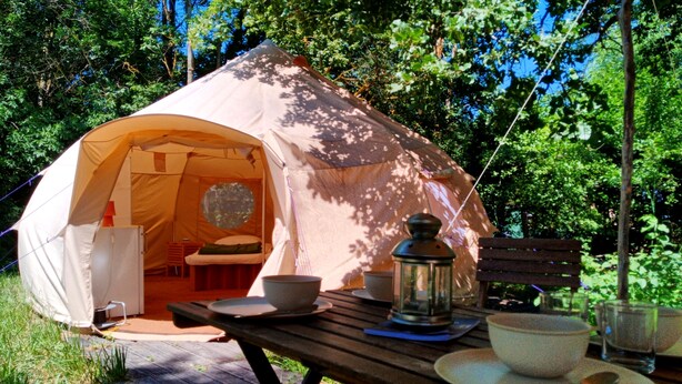Een tent met een rond raam, een tafel met kommen en een lantaarn, en een bank.